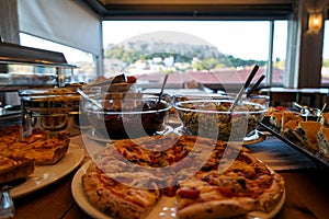 Greek breakfast buffet table full with varieties of food with pizza foreground and Acropolis view from afar