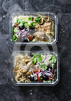 Greek chicken grain lunch box. Lemon herbs chicken, couscous, vegetables, olives, feta cheese lunch box on dark background, top