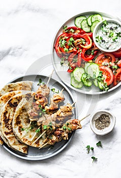 Greek chicken skewers, flatbread, tomatoes, cucumber salad, baked sweet pepper, tzatziki yogurt herb sauce on a light background,