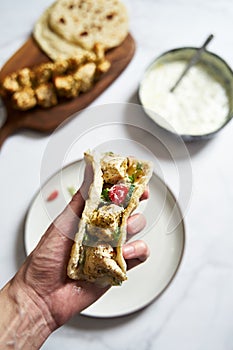 Greek chicken souvlaki ona pita with fresh vegetables with tzatziki sauce. Hand holding one pita with chicken souvlaki