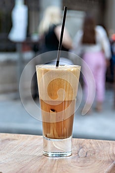 A greek cold coffee, freddo cappuccino placed on a wooden table outdoors.