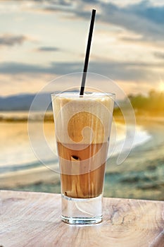 A greek cold coffee, freddo cappuccino placed on a wooden table over a beach background.