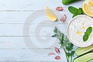 Greek dip sauce or dressing tzatziki from sour cream yogurt decorated with olive oil and mint on wooden table top view.