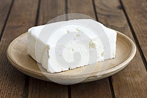 Greek feta cheese block on rustic plate and table.