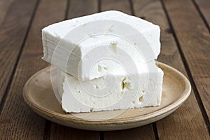 Greek feta cheese block on rustic plate and table.