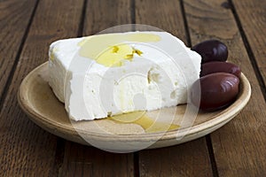 Greek feta cheese, oil, kalamata olives on rustic plate board.