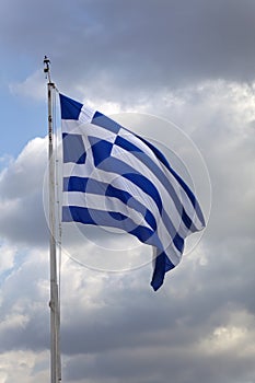 Greek flag on a flagpole against dark clouds