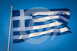 Greek flag fluttering in sunshine against blue sky