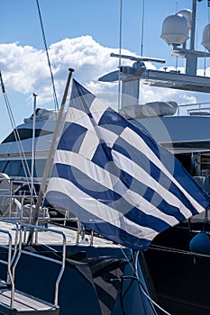 Greek flag on pole on ferry`s stern. Ongoing cruise to islands. Blue sky background, close up view photo