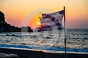 Greek flag waving at sunset on a sandy beach in Crete, Greece