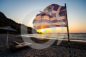 Greek flag waving at sunset on a sandy beach in Crete, Greece