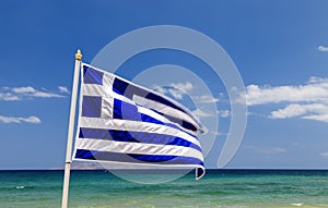 Greek flag waving in wind in blue sky and white clouds and sea waves around