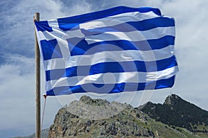Greek flag waving in the wind and mount Tsambika