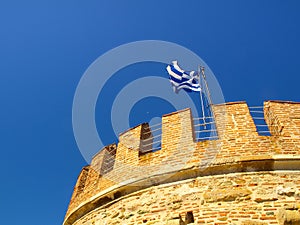 The greek flag on The White Tower of Thessaloniki on the shore of The Aegean Sea, Thessaloniki, Greece