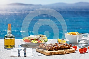 Greek food concept with farmers salad and souvlaki skewers in front of the Aegean sea