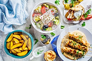Greek food: greek salad, chicken souvlaki, gyros and baked potato wedges on gray background, top view. Traditional greek cuisine