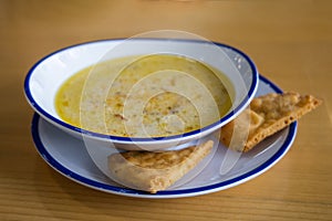 Greek food lemon chicken soup in a bowl the winter on a restaurant dining table with fried pita crisp crackers as a