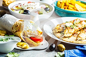 Greek food: salad, chicken souvlaki, gyros and baked potatoes on gray background. Traditional greek cuisine concept
