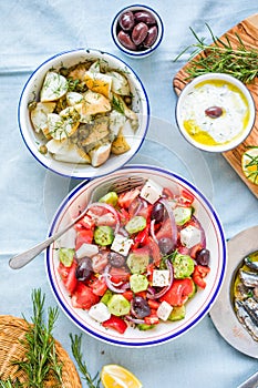 Greek food table scene, top view . Variety of items including greece salad, cucumber dip Tzatziki, Anchovy fillets, lemon potatoes