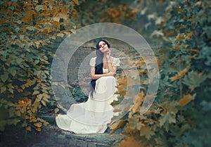 Greek goddess sits on the stone steps in autumn forest, light skin, white long elegant dress, like a sculpture, black