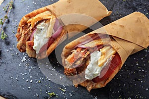 Greek gyros wrapped in pita breads on a black dish