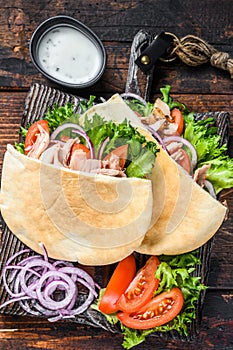 Greek gyros wrapped in pita breads with vegetables and sauce. Dark wooden background. Top view