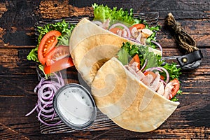 Greek gyros wrapped in pita breads with vegetables and sauce. Dark wooden background. Top view