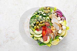 Greek inspired salad with grilled chicken meat, vegetables and feta cheese in a bowl on a table, with olive oil dressing