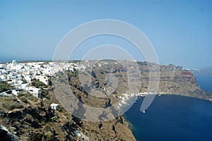 Greek island of Thirasia near to Santorini. View of cliffs and a bay with the old town of Manolas on the sky line.