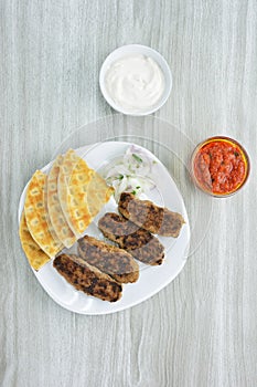 Greek Kebabs, pita bread ,chopped onion in plate and yogurt and tomato sauce in bowls