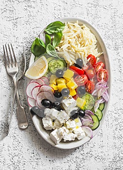 Greek lemon orzo salad. Feta, orzo, tomatoes, cucumbers, radishes, olives, peppers salad on a light background, top view. Healthy