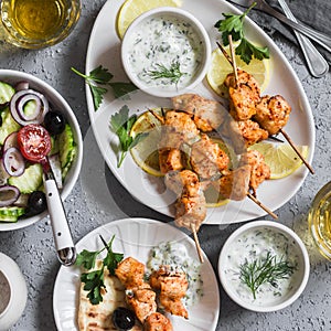 Greek lunch - chicken kebabs, greek salad, tzatziki, flatbreads and white wine. On a light background