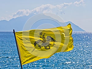 Greek navy flag on a ship which sails near greek coast of aegean sea with holy mountain Athos in background