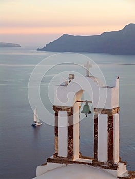 Greek Orthodox Church Bell Tower against Aegean Sea with Sailing Boat at the Sunset, Santorini