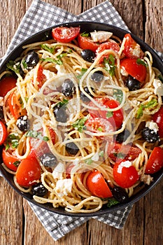 Greek pasta spaghetti salad with feta, olives, tomatoes and herbs close-up on a plate. Vertical top view