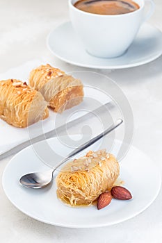 Greek pastry Kataifi with shredded filo dough stuffed with almond nuts, in honey syrup, on white plate, served with cup of coffee