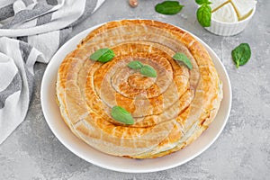 Greek pie spanakopita with feta cheese and spinach on a white plate on a gray concrete background. Copy space