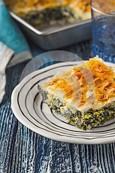 Greek pie spanakopita in the white plate on the blue wooden table