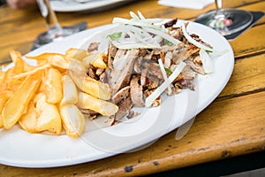 Greek pork meat Gyros with onions, Tsatsiki and French fries on wooden table in restaurant