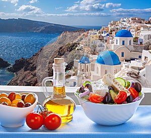 Greek salad against famous church in Oia village, Santorini island in Greece