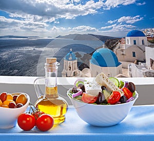 Greek salad against famous church in Oia village, Santorini island in Greece