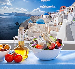 Greek salad against famous church in Oia village on Santorini island in Greece