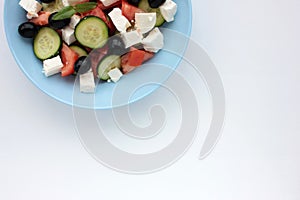 Greek salad in blue bowl on white background. Close-up of vegetable salad with fets cheese, black olives, cucumber and tomatoes.