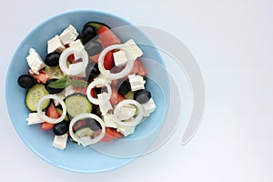 Greek salad in blue bowl on white background. Close-up of vegetable salad with fets cheese, black olives, cucumber and tomatoes.