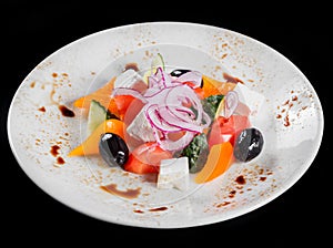 Greek salad in a bowl with fresh vegetables and feta cheese, isolated on black background. Top view