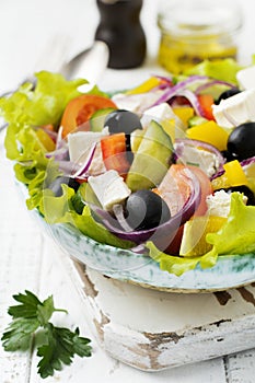 Greek salad in a ceramic plate on a white wooden background. Traditional Greek dish. Selective focus.Top view