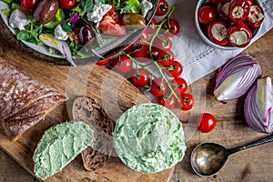 Greek salad with cherry tomatoes, onions, antipasti, spoon and moretum Roman pesto on wooden table top view