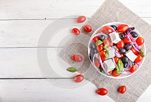 Greek salad with fresh cherry tomatoes, feta cheese, black olives, basil and onion on white wooden background