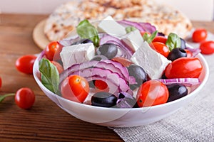 Greek salad with fresh cherry tomatoes, feta cheese, black olives, basil and onion on wooden background