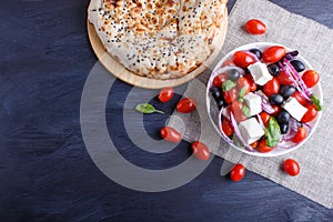 Greek salad with fresh cherry tomatoes, feta cheese, black olives, basil and onion on black wooden background